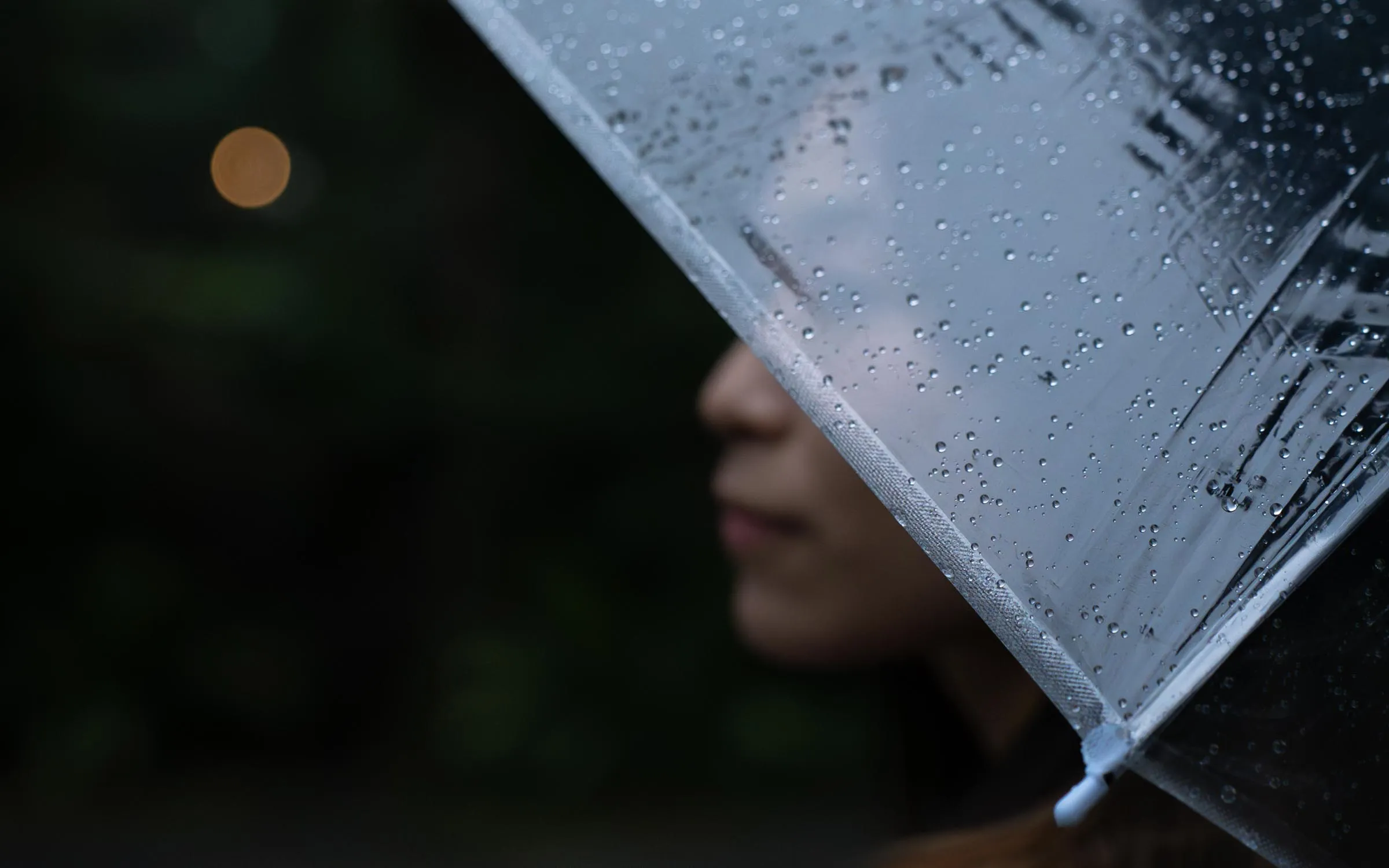 雨中一把透明的伞，水珠挂在伞沿，伞下的人安静地望着远方，路灯晕成一片暖黄